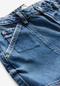Denim lühikesed püksid klassikalise sinise värviga, kulunud servaga, viie taskuga, hõbedase riistvaraga ja kontrastse kollase tikandiga.