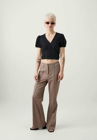 Top preto cropped com mangas bufantes, combinado com calças flare de cintura alta em bege. Modelo usa óculos de sol e tem cabelo curto.