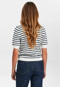 Īsām piedurknēm, ribota džemperis baltā krāsā ar tumši ziliem svītrām, ar viļņotu apakšmalu. Piedāvāts kopā ar augstām, tumši zilām džinsa biksēm.