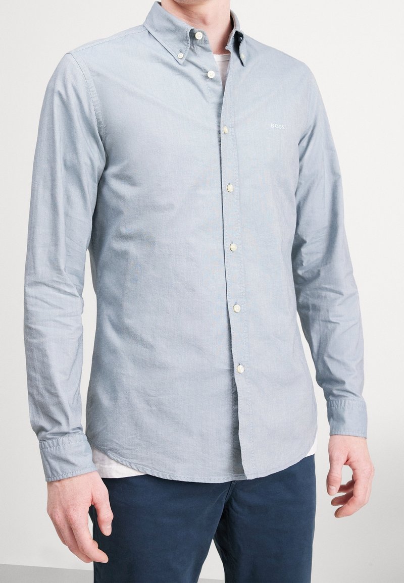 Ljusblå skjorta med knappar i ett strukturerat tyg, med klassisk krage, vita knappar och en liten logotyp på bröstet.