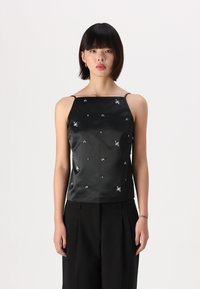 Black satin camisole with spaghetti straps, featuring scattered rhinestone embellishments across the fabric, styled with black trousers.