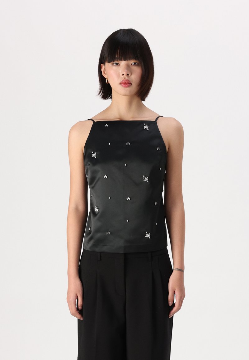 Black satin camisole with spaghetti straps, featuring scattered rhinestone embellishments across the fabric, styled with black trousers.