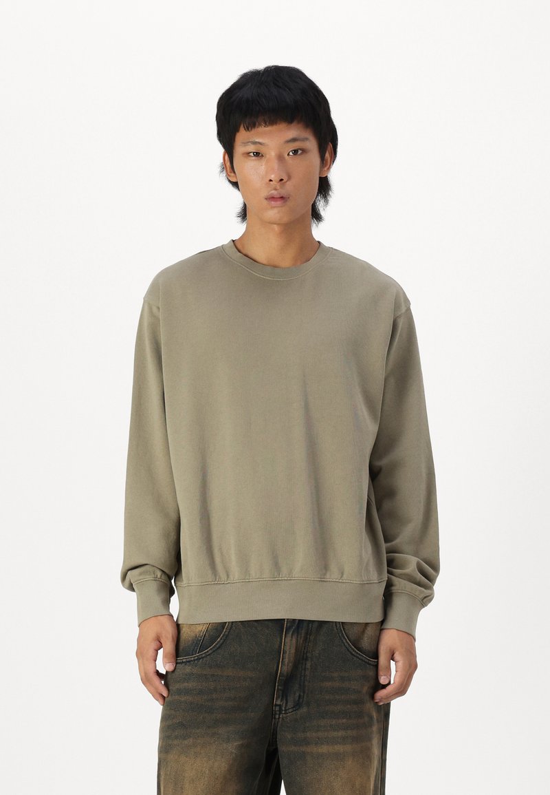Olijfgroene crewneck sweatshirt met ribbelmanchetten en -zoom, gemaakt van zacht katoen. Gedeeltelijk gedragen met vervaagde denim broek.