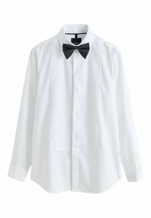Man with long dreadlocks wearing a white dress shirt and black dress pants, viewed from the back against a plain background.