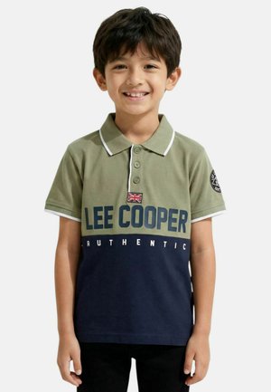 Garçon souriant, portant un polo à manches courtes avec le haut vert olive, le bas bleu marine, le drapeau britannique et le texte « LEE COOPER AUTHENTIC ».
