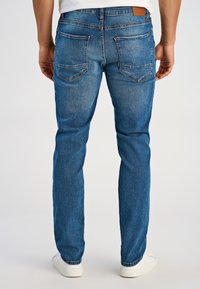 Niebieskie jeansy z denimu o prostym kroju, z tylnymi kieszeniami, delikatnym wyblaknięciem oraz skórzaną naszywką na pasku. Noszone z białymi butami.