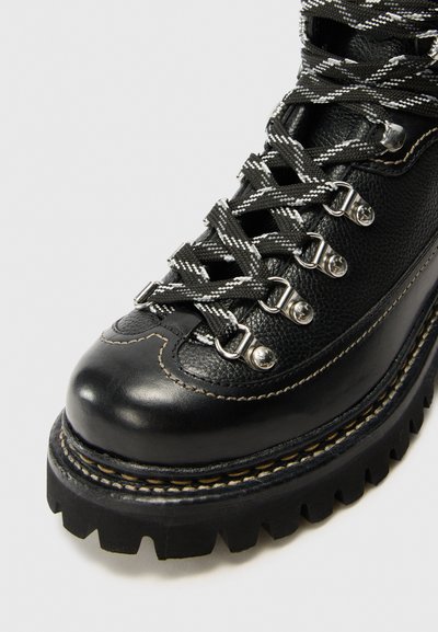 Bota de senderismo de cuero negro con ojales plateados, suela de goma gruesa y parte superior texturizada con costuras en contraste y cordones en blanco y negro.