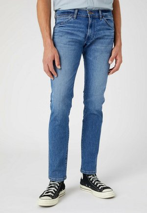 Blauwe denim jeans met een slim fit, voorzien van een klassiek vijf-pocket ontwerp en contrasterende stiksels. Gepaard met zwarte high-top sneakers.