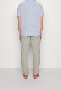 Ljusblå skjorta med kort ärm, beige linnebyxor och röda kanvas sneakers. Skjortan har en krage och knäppning.