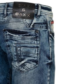 Blauwe denim jeans met een vervaagd uiterlijk, voorzien van achterzakken en een zwart leren label met de tekst "CIPO & BAXX." Gestikte details zijn zichtbaar.
