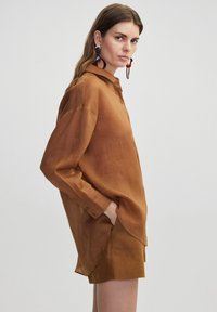 Brown button-up shirt with long sleeves, soft texture, side slits, and a rounded hem, paired with matching shorts.