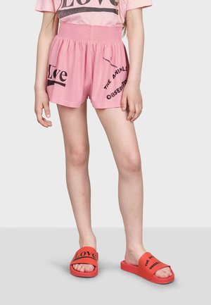 T-shirt en coton rose avec impression "Love", assorti à un short rose avec du texte noir. Sandales rouges avec imprimé "Love" sur les brides.