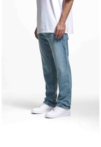 Světle modré džíny rovného střihu s viditelným šitím, nošeny s jednoduchým bílým tričkem a bílými teniskami. Klasický neformální outfit.