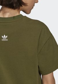 Olivgrön t-shirt i bomull med korta ärmar, med en liten vit broderad logotyp på baksidan nära kragen och en rund halsringning.