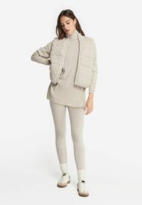 Pull en tricot beige avec un motif texturé, associé à un haut côtelé assorti et des leggings. Des baskets blanches réfléchissantes complètent le look.