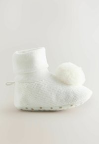 Chausson en tricot blanc avec un revers replié, doté d'un accent pom-pom duveteux et d'une semelle texturée avec de petits points.