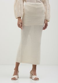 Jupe midi en tricot de couleur crème avec un motif texturé et rayé, dotée d'une taille élastique, associée à des chaussures à talons blocs ouvertes beiges.