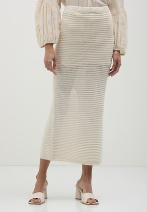 Gonna midi lavorata a maglia di colore crema con un motivo a righe testurizzato e una vita elastica, abbinata a scarpe con tacco a blocco beige con punta aperta.
