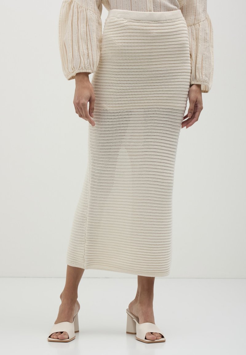 Jupe midi en tricot de couleur crème avec un motif texturé et rayé, dotée d'une taille élastique, associée à des chaussures à talons blocs ouvertes beiges.