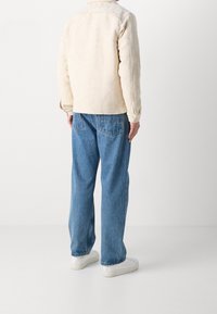 Fleecejacka i ljusbeige med texturerad yta, knappmanchetter och krage, tillsammans med blå denimjeans och vita sneakers.