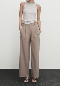 Haut sans manches gris avec texture côtelée, associé à un pantalon beige taille haute à jambes larges comportant deux poches latérales et des boutons décoratifs.