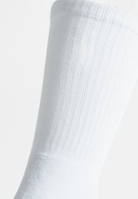 Calza in cotone bianco a costine con una texture liscia, lunghezza fino al polpaccio, dotata di una vestibilità aderente e senza motivi o accenti visibili.