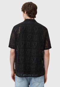 Camisa negra de manga corta con una textura similar al encaje, con un patrón en cuadrícula de símbolos y letras, y un ajuste relajado.