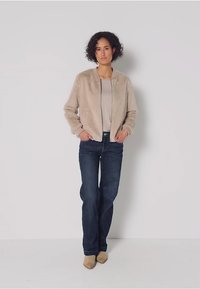 Faux fur bomberjacka i beige, med dragkedja fram, ribbade ärmar, bärs över en ljus topp och mörk denimjeans, med beiga ankelskor.