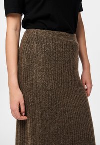 Jupe beige côtelée, longueur mi-mollet, dotée d'une taille ajustée et d'une texture douce. Associée à un top noir à manches courtes.