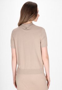 Beige kortærmet sweater med høj krave, ribbet kant og glat, tekstureret stof. Har et lille logo på bagsiden.