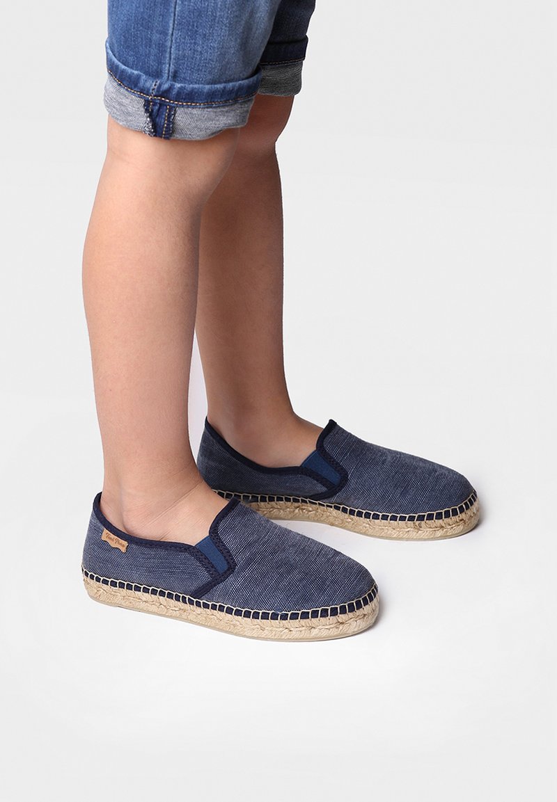 Tamno plava platnena slip-on obuća s pletenim juta đonom, koja ima kontrastnu tamnoplavu obrub i mali logotip na strani.