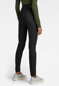 Černé džíny s vysokým pasem a přiléhavou siluetou, které mají dvě zadní kapsy a decentní švy, doplněné šedými botami.