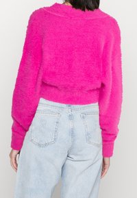 Flauschiger rosa Pullover mit lässiger Passform, geripptem Rundhalsausschnitt und Ballonärmeln, kombiniert mit hellblauen hochgeschnittenen Jeans.