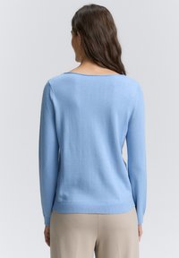 Hellblau gestrickter Pullover mit langen Ärmeln, Rundhalsausschnitt und geripptem Saum. Sanfte Textur, minimale Details, figurbetonte Silhouette.