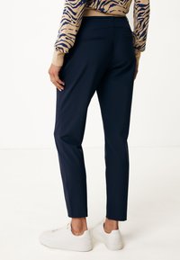 Pantalones de corte entallado en azul marino, con bolsillos traseros y longitud ligeramente cortada, combinados con zapatillas blancas.