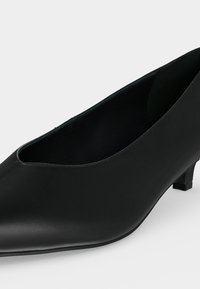Chaussure de ville noire pour femme à talon bas, bout pointu, finition lisse et talon carré discret.