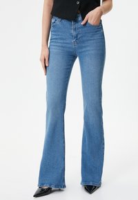 Jeans acampanados azules de tela de mezclilla, de talle alto con cinco bolsillos, con un diseño clásico y un acabado de lavado claro.