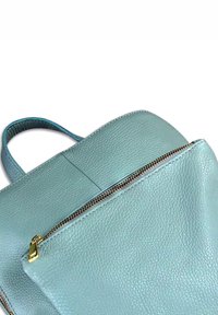 Sac à dos en cuir bleu clair avec une surface texturée et une fermeture éclair dorée partiellement ouverte sur fond blanc.
