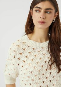 Tröja i stickat i cremefärg med ett mönster av öppna maskor. Har en bred halsringning och korta ärmar med manchetter.