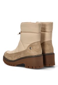 Botasankle beige con parte superior acolchada y acentos de ante, que presentan una gruesa suela de goma marrón y costuras decorativas.