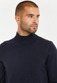 Maglione a collo alto blu navy realizzato in morbido tessuto lavorato a maglia; design aderente con colletto alto a coste e maniche lunghe.
