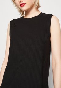 Top nero senza maniche con texture a costine, scollo rotondo e sottili dettagli di cucitura. Tessuto leggero con una silhouette aderente.