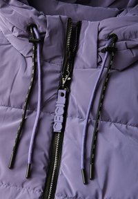 Chaqueta de plumas morada con un tejido duradero, un cierre completo con un acento negro y cordones morados con puntas negras.