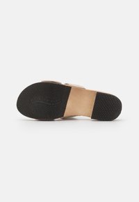 Semelle de sandale beige avec un dessous en caoutchouc noir texturé. Équipée d'un dessus lisse de couleur claire avec deux sangles ajustables.