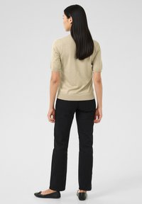 Lühikeste varrukatega helebeež kootud kampsun, millel on mustad püksid; sile pind ja keha järgnev lõige, vaadatuna tagantpoolt.