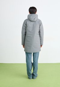 Grå isoleret parka med hætte, der har en lige skæring og glat tekstur, parret med blå jeans. Synlige syninger.