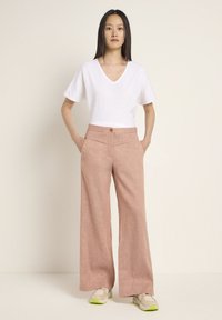 Lightweight white V-neck T-shirt paired with pink, wide-leg trousers featuring a textured fabric and a front button closure.