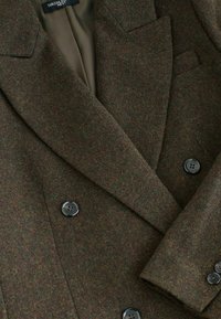 Brun houndstooth dobbeltbrystet blazer lavet af tekstureret stof, med sorte knapper og skarpe slag. Inderlinningen er olivengrøn.