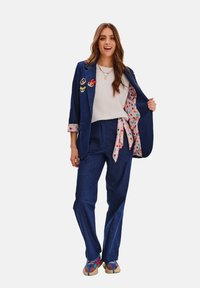 Džínový oblek v tmavě modré barvě s barevnou podšívkou s puntíky. Obsahuje přiléhavý blazer s kapsou a volné kalhoty doplněné barevnými botami.