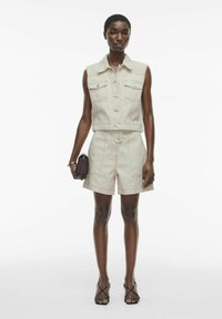 Conjunto de dos piezas de mezclilla beige, top corto sin mangas con cuatro bolsillos, pantalones cortos a juego, costuras detalladas, acompañado de un bolso pequeño y sandalias.